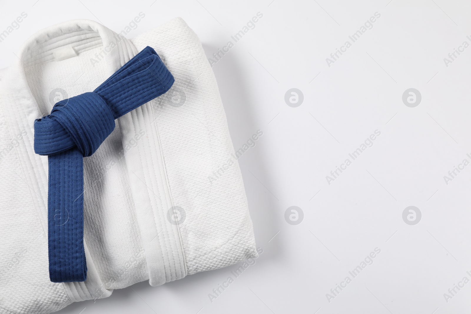 Photo of Blue karate belt and kimono on white background, top view. Space for text