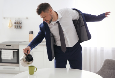 Photo of Man pouring coffee into cup in hurry at home. Morning preparations