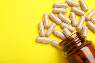 Photo of Many gelatin capsules and bottle on yellow background, flat lay. Space for text