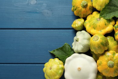 Photo of Fresh ripe pattypan squashes with leaves on blue wooden table, flat lay. Space for text