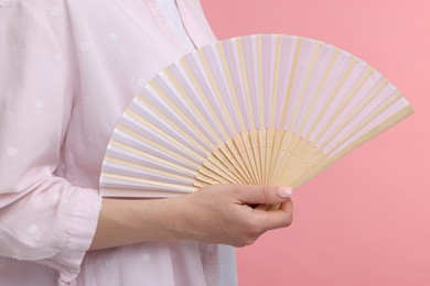 Woman with hand fan on pink background, closeup