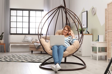 Young woman working with laptop on hanging armchair in home office