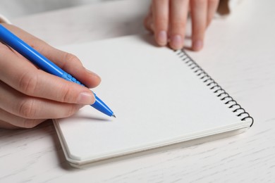 Photo of Woman writing in notebook with pen at white wooden table, closeup