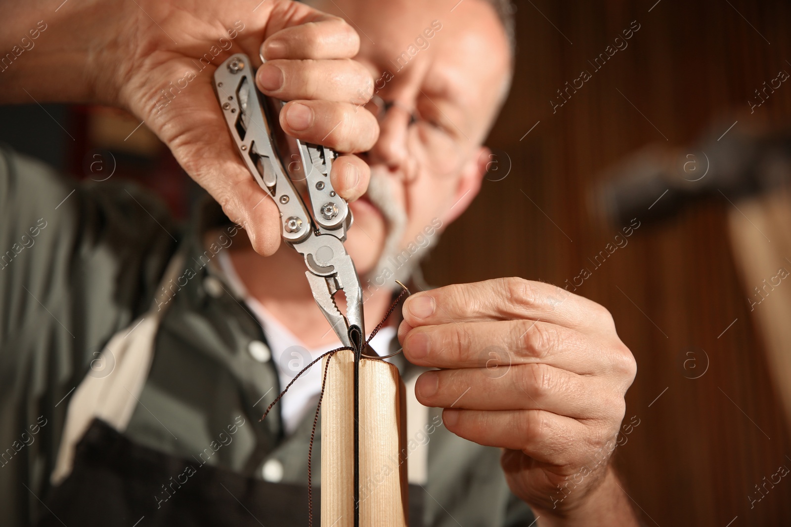 Photo of Man sewing piece of leather in workshop, closeup