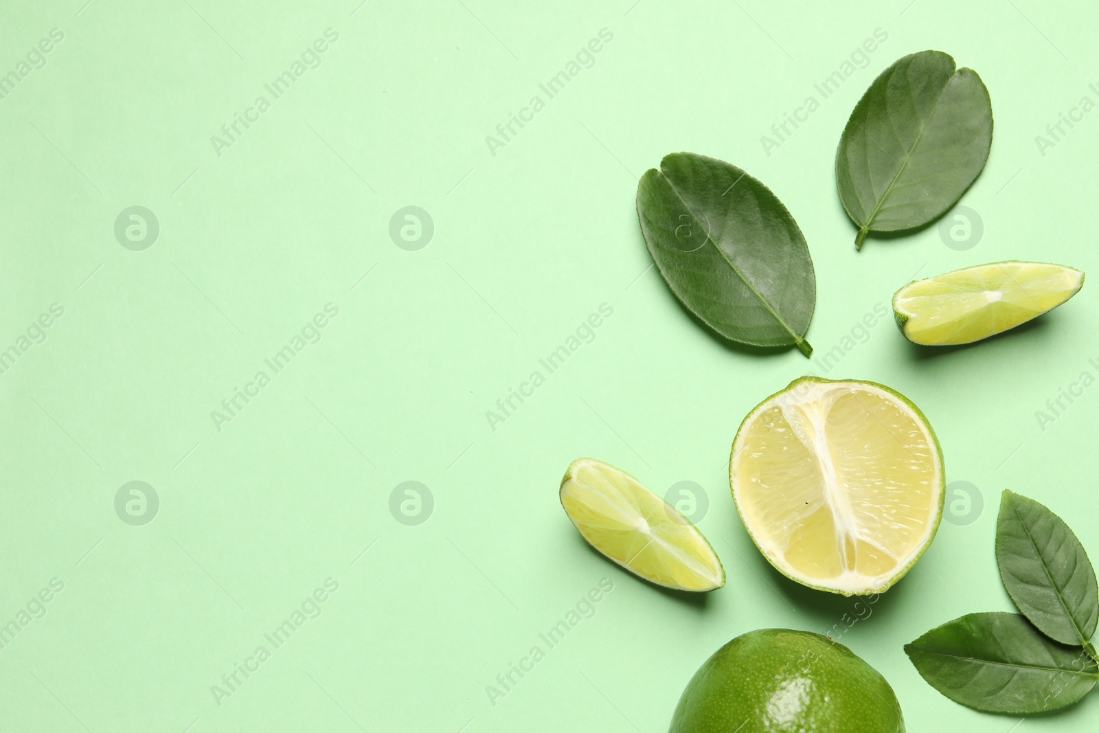 Photo of Whole and cut fresh ripe limes with leaves on light green background, flat lay