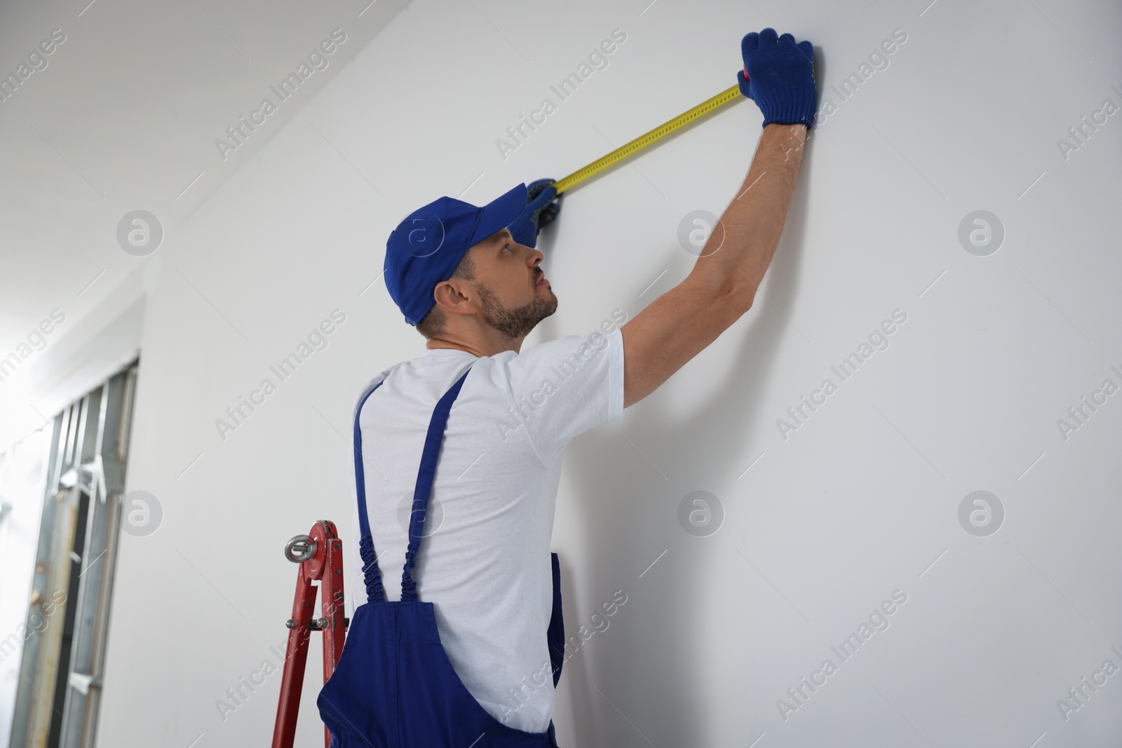Photo of Construction worker using measuring tape in room prepared for renovation
