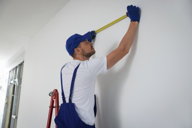 Construction worker using measuring tape in room prepared for renovation