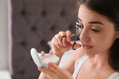 Attractive young woman curling her eyelashes indoors