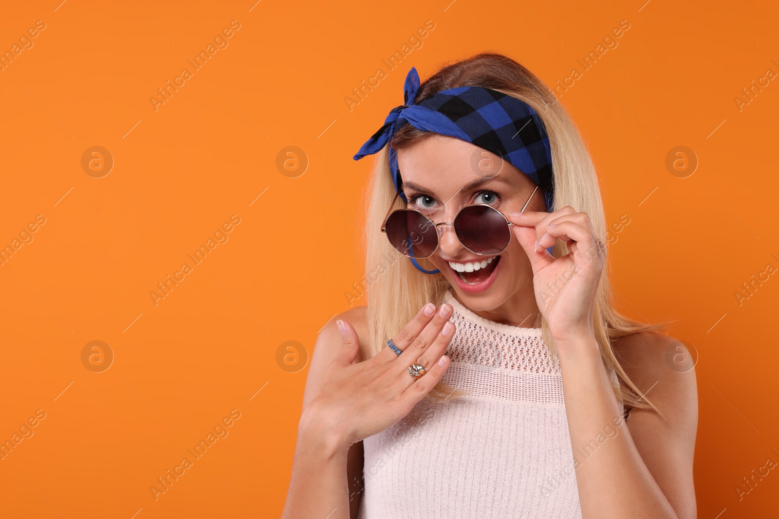 Photo of Portrait of smiling hippie woman in sunglasses on orange background. Space for text