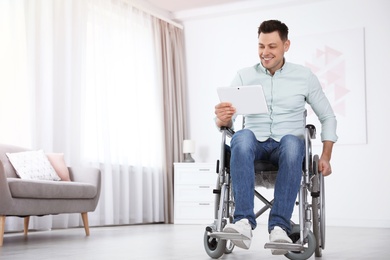 Happy man with tablet sitting in wheelchair at home