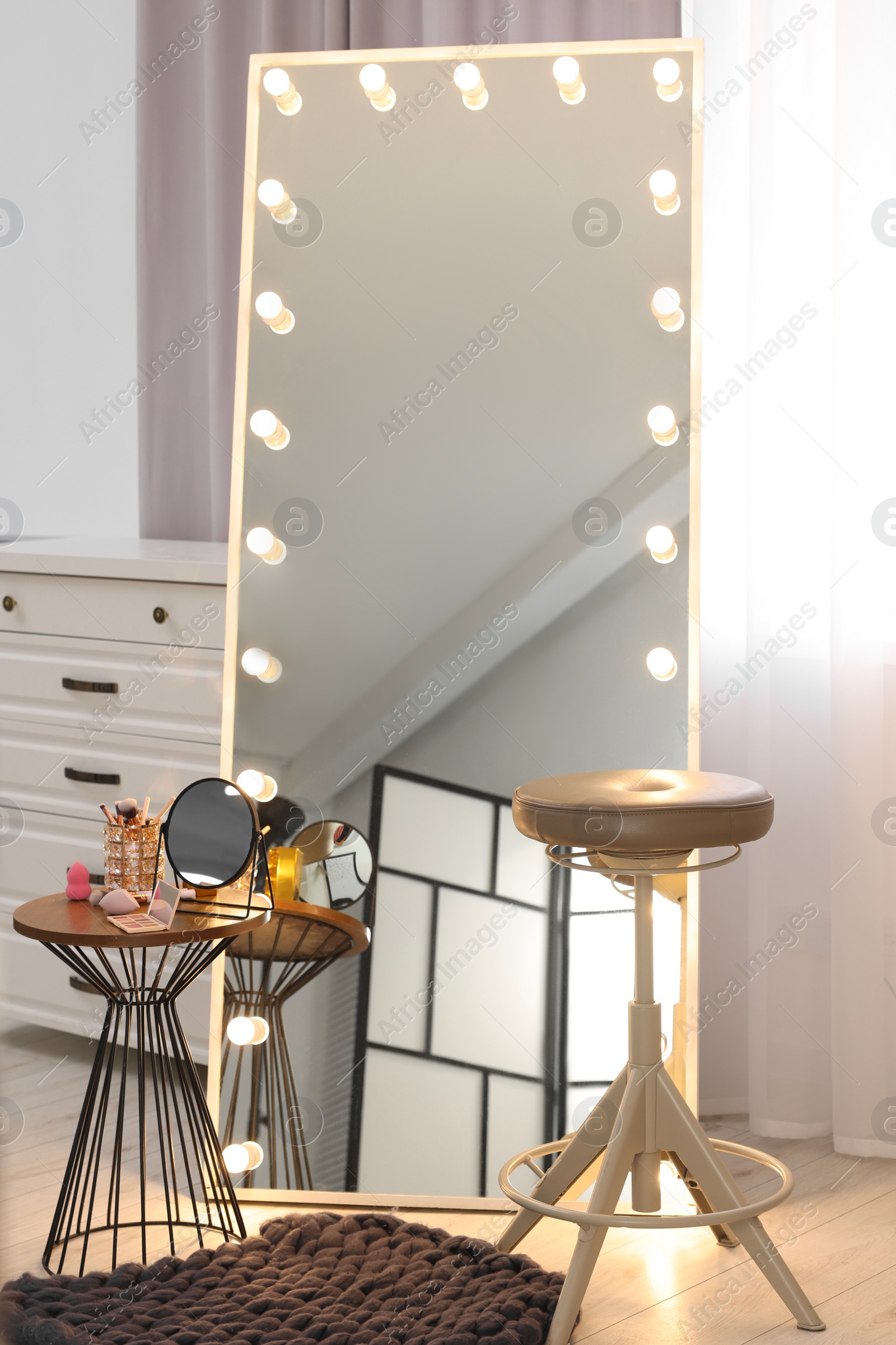 Photo of Makeup room. Stylish mirror with light bulbs, beauty products on table and chair indoors