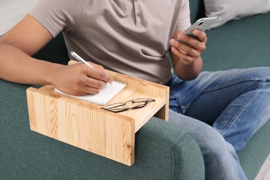 Photo of Man writing in notebook on sofa armrest wooden table at home, closeup