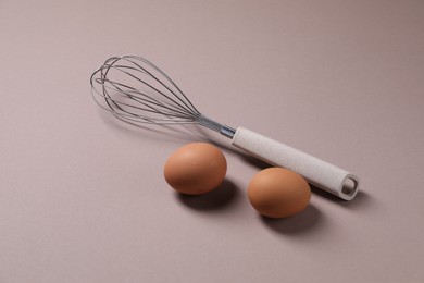 Photo of Metal whisk and raw eggs on grey background