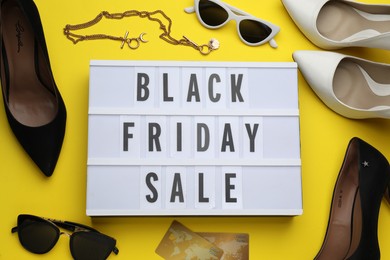 Photo of Light box with text Black Friday Sale, women's accessories, shoes and credit cards on yellow background, flat lay