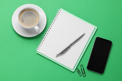 Ballpoint pen, notebook and smartphone on green background, flat lay