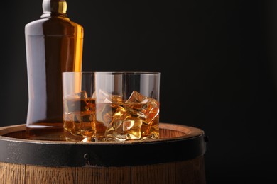 Photo of Whiskey with ice cubes in glasses and bottle on wooden barrel against black background