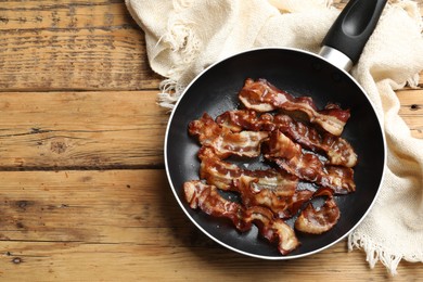 Delicious bacon slices in frying pan on wooden table, top view. Space for text