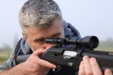 Man aiming with hunting rifle outdoors, closeup