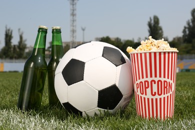 Photo of Football ball with beer and popcorn on green field grass in stadium