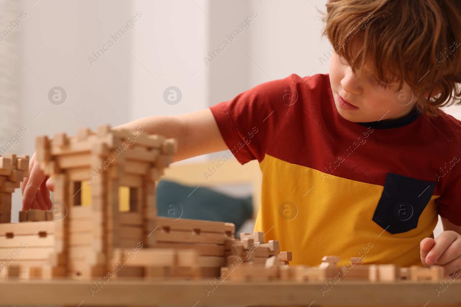 Photo of Little boy playing with wooden entry gate at table in room. Child's toy