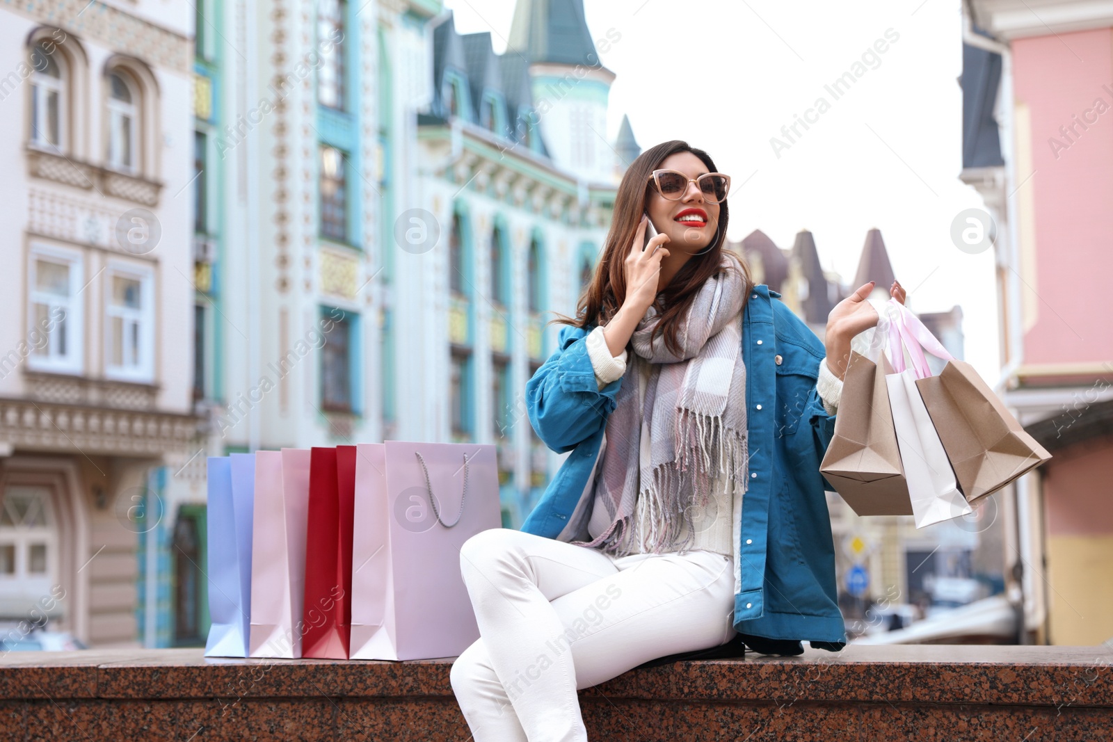 Photo of Beautiful young woman with shopping bags talking on smartphone outdoors