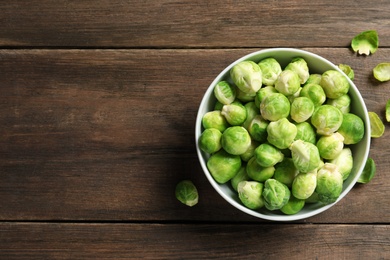 Photo of Bowl of fresh Brussels sprouts and leaves on wooden background, top view with space for text