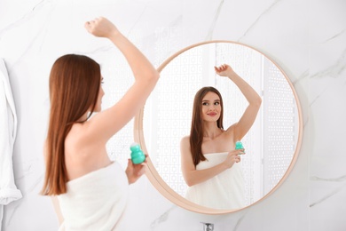 Beautiful young woman applying deodorant after shower in bathroom