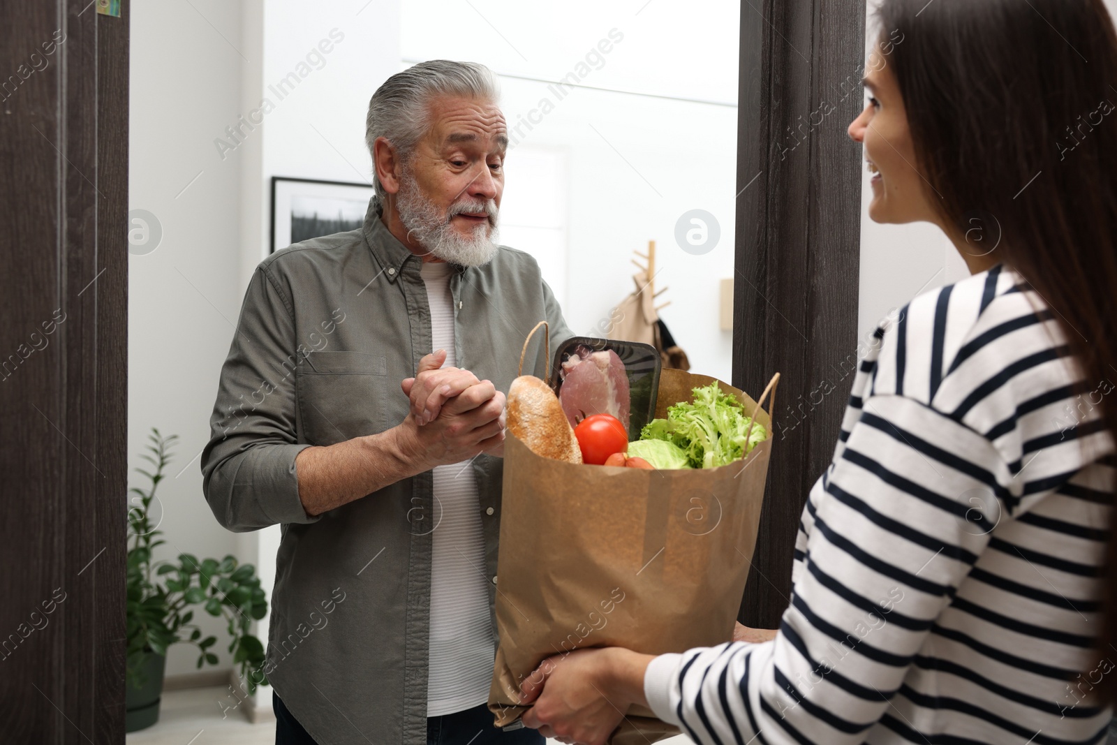 Photo of Courier giving paper bag with food products to senior man indoors