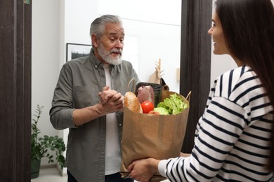 Photo of Courier giving paper bag with food products to senior man indoors