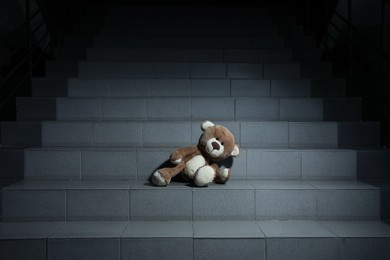 Photo of Lonely teddy bear on grey stairs indoors