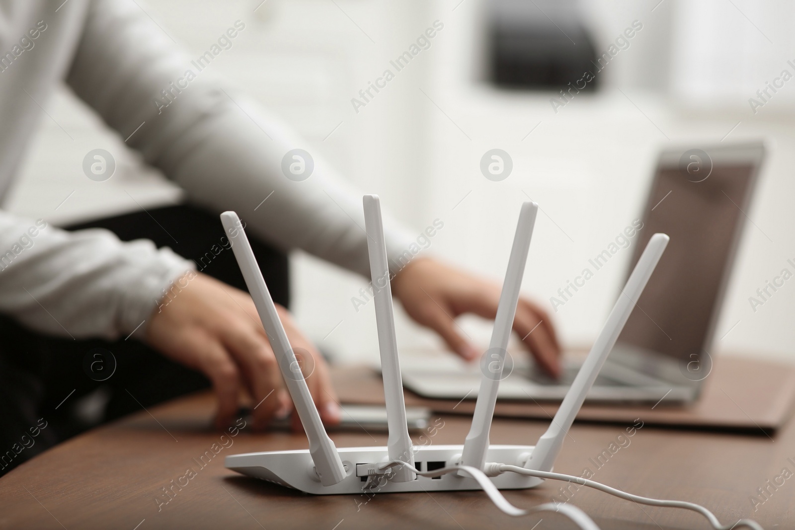 Photo of Man with laptop and smartphone working at wooden table, focus on Wi-Fi router