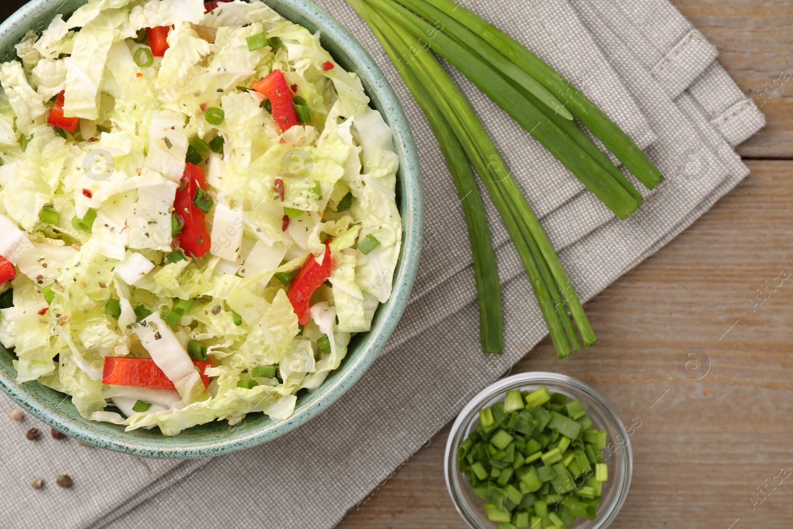 Photo of Tasty salad with Chinese cabbage in bowl and green onion on wooden table, top view