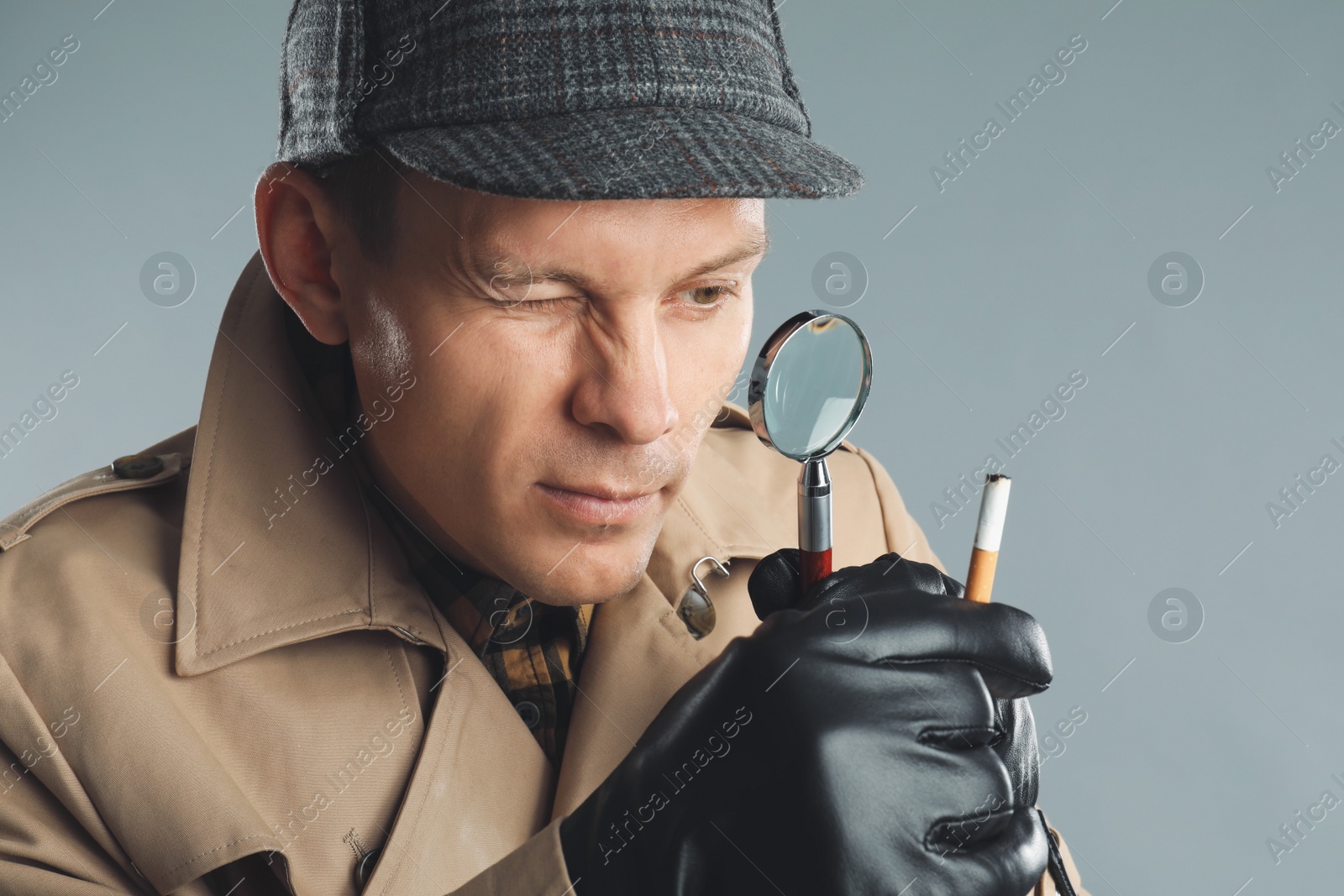 Photo of Male detective exploring cigarette stub with magnifying glass on grey background