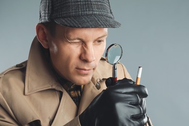 Photo of Male detective exploring cigarette stub with magnifying glass on grey background