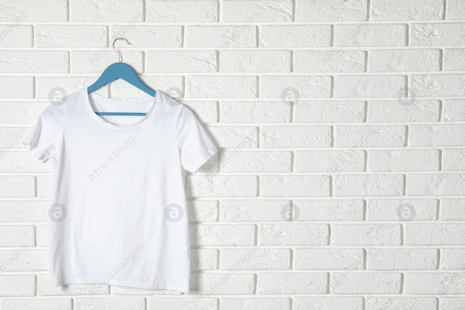 Photo of Hanger with white t-shirt against brick wall. Mockup for design