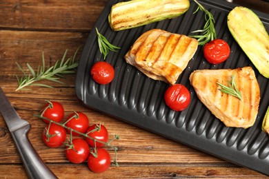 Photo of Electric grill with tasty meat, rosemary and vegetables on wooden table