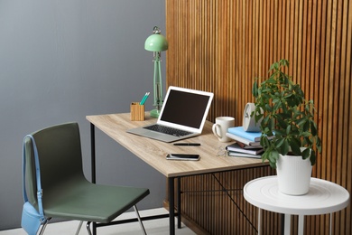 Photo of Stylish workplace interior with laptop on table near wooden wall. Space for text