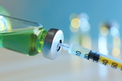 Photo of Filling syringe with medication from vial against blurred background, closeup. Vaccination and immunization