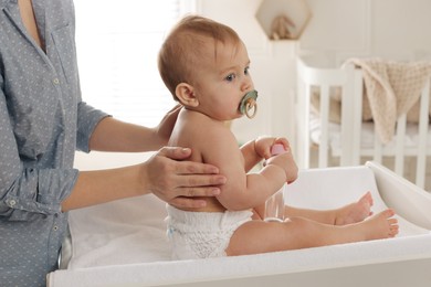 Photo of Mother massaging her cute baby with oil on changing table at home, closeup