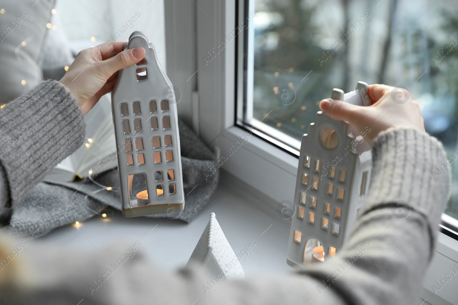 Photo of Woman with beautiful house shaped candle holders near window indoors, closeup