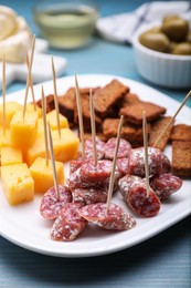 Photo of Toothpick appetizers. Pieces of sausage, cheese and croutons on light blue wooden table