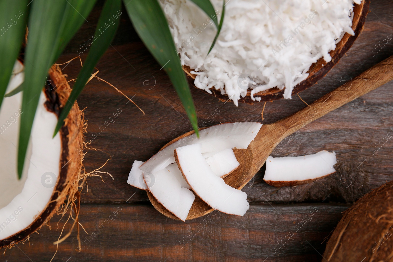 Photo of Coconut flakes, spoon and nut on wooden table, flat lay