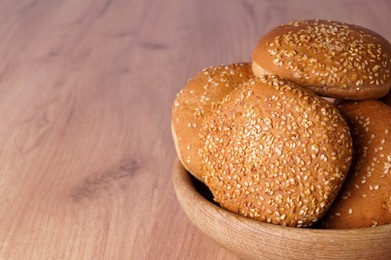 Photo of Bowl of fresh buns with sesame seeds on wooden table, closeup. Space for text