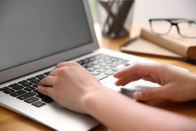 Woman working with modern laptop at wooden table, closeup