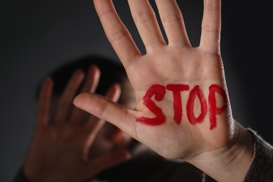 Photo of Woman with word Stop written on hand against black background, closeup. Domestic violence concept