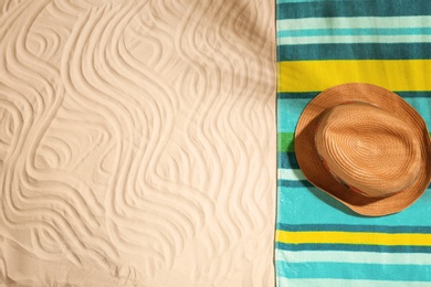 Bright towel and hat on sand, top view with space for text. Beach objects