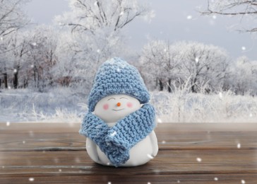 Image of Cute decorative snowman in blue hat and scarf on wooden table outdoors