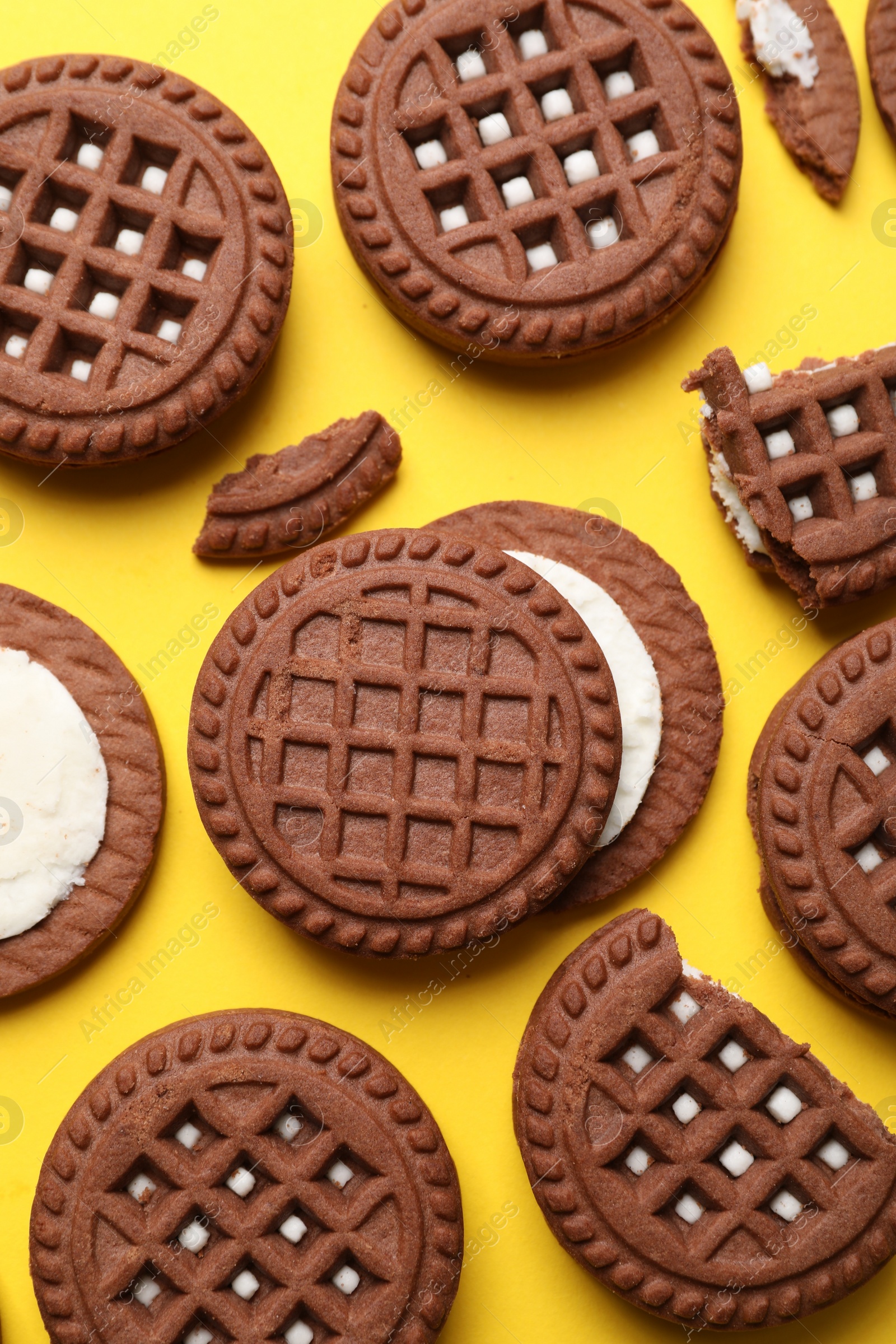 Photo of Tasty chocolate sandwich cookies with cream on yellow background, flat lay