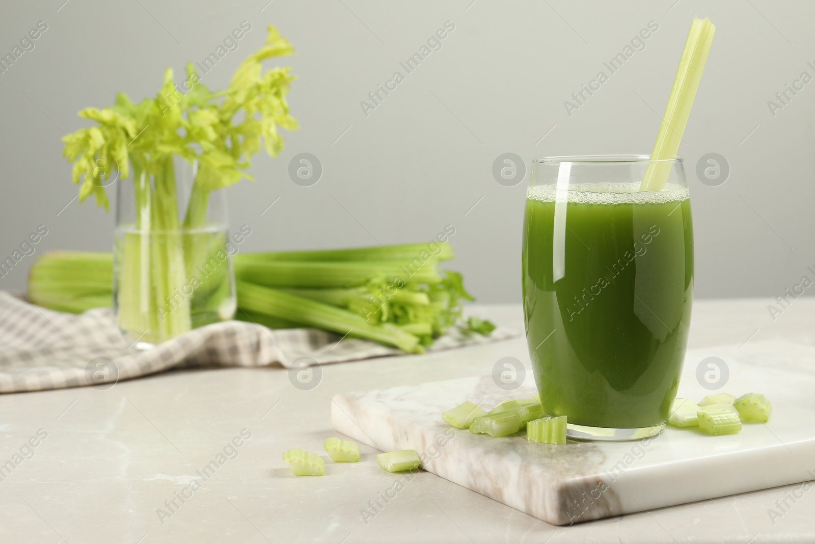 Photo of Glass of celery juice and fresh vegetables on light gray table, space for text