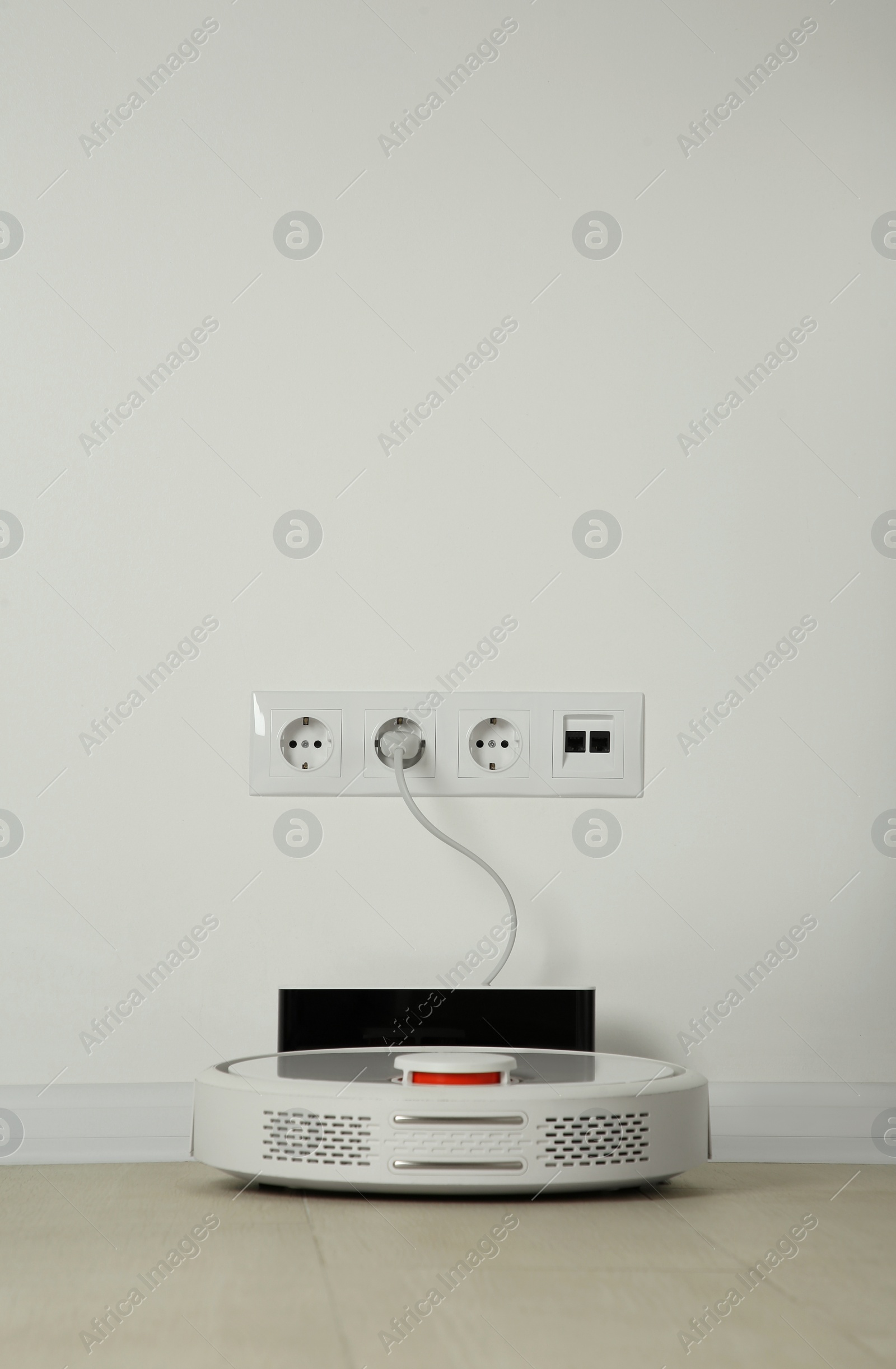 Photo of Robotic vacuum cleaner charging from electric socket on floor indoors